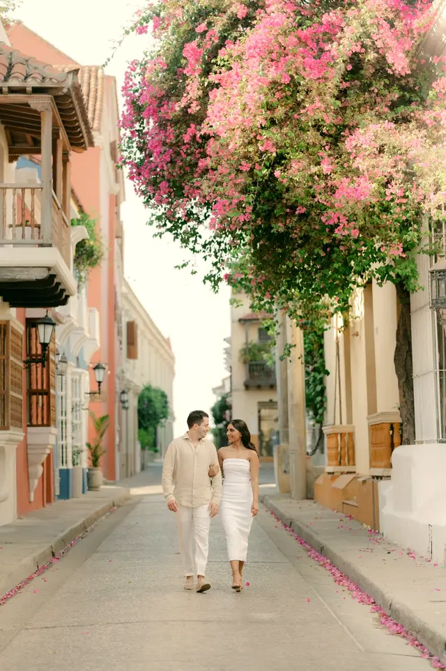 Pareja de novios caminando bajo buganvilias rosadas en una calle colonial