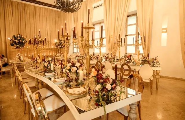 Mesa de espejo con candelabros dorados y flores en tonos rojos