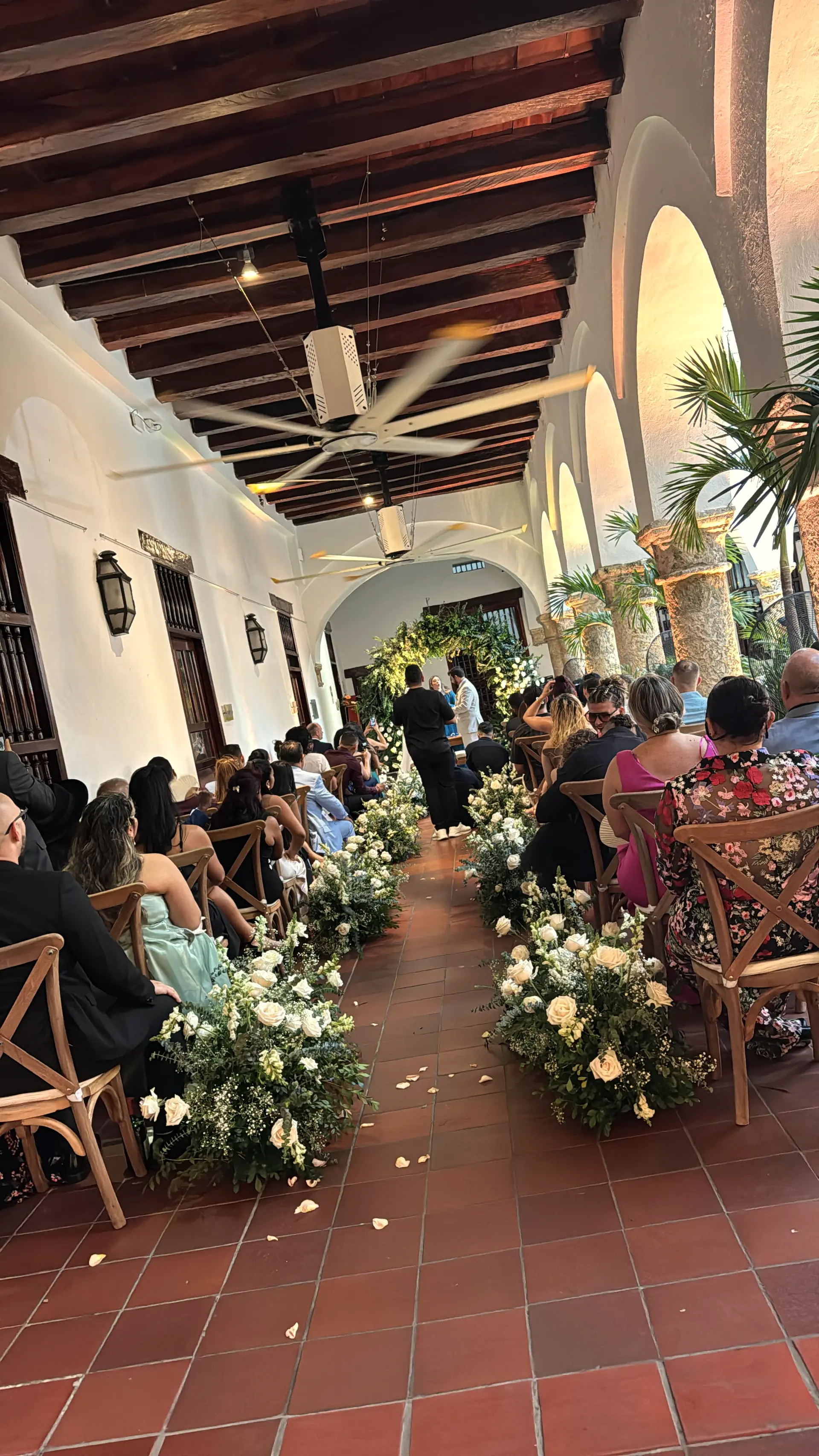 Ceremony aisle in a colonial courtyard with seated guests and flower arrangements