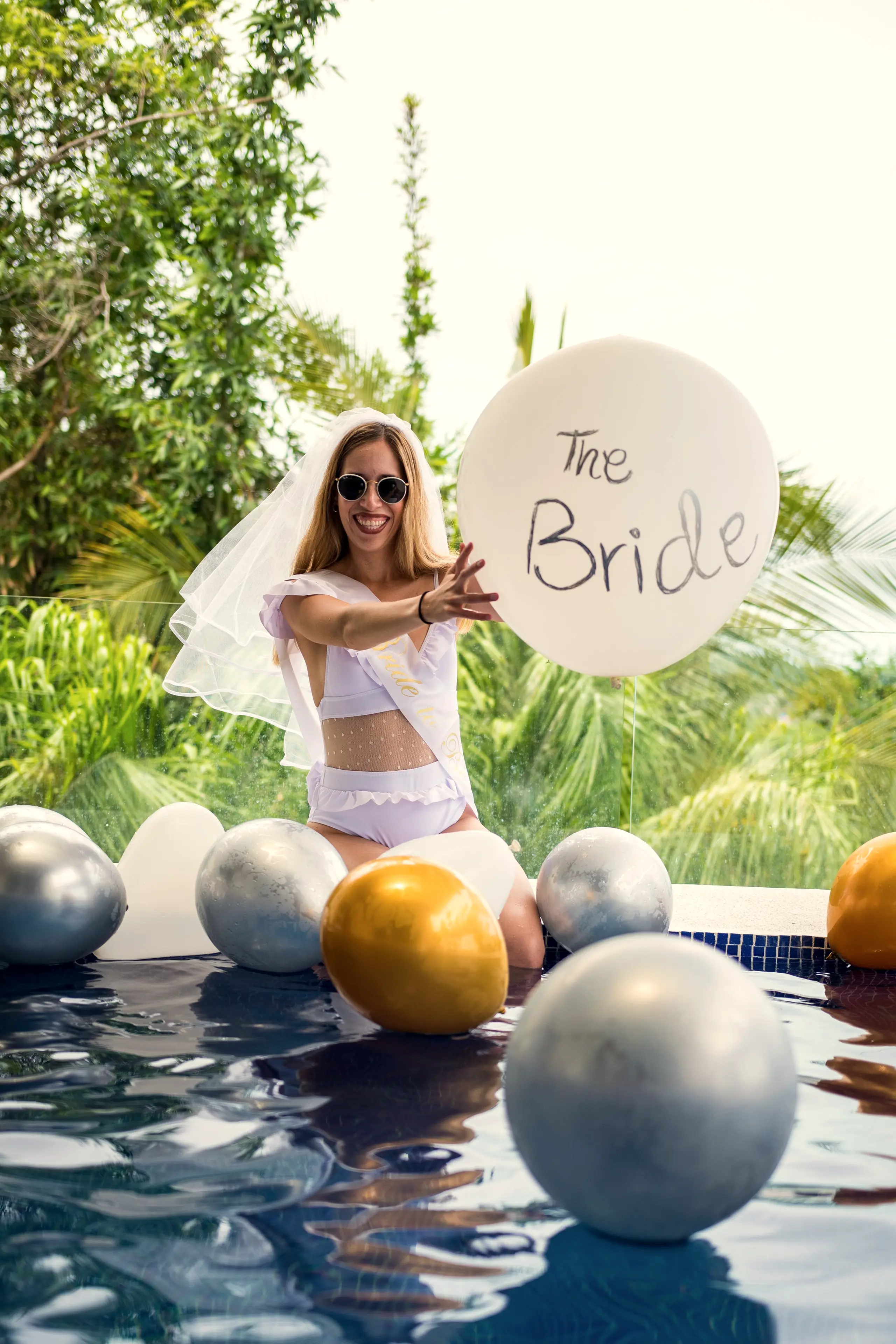 Bride in a veil with a balloon reading The Bride beside a pool