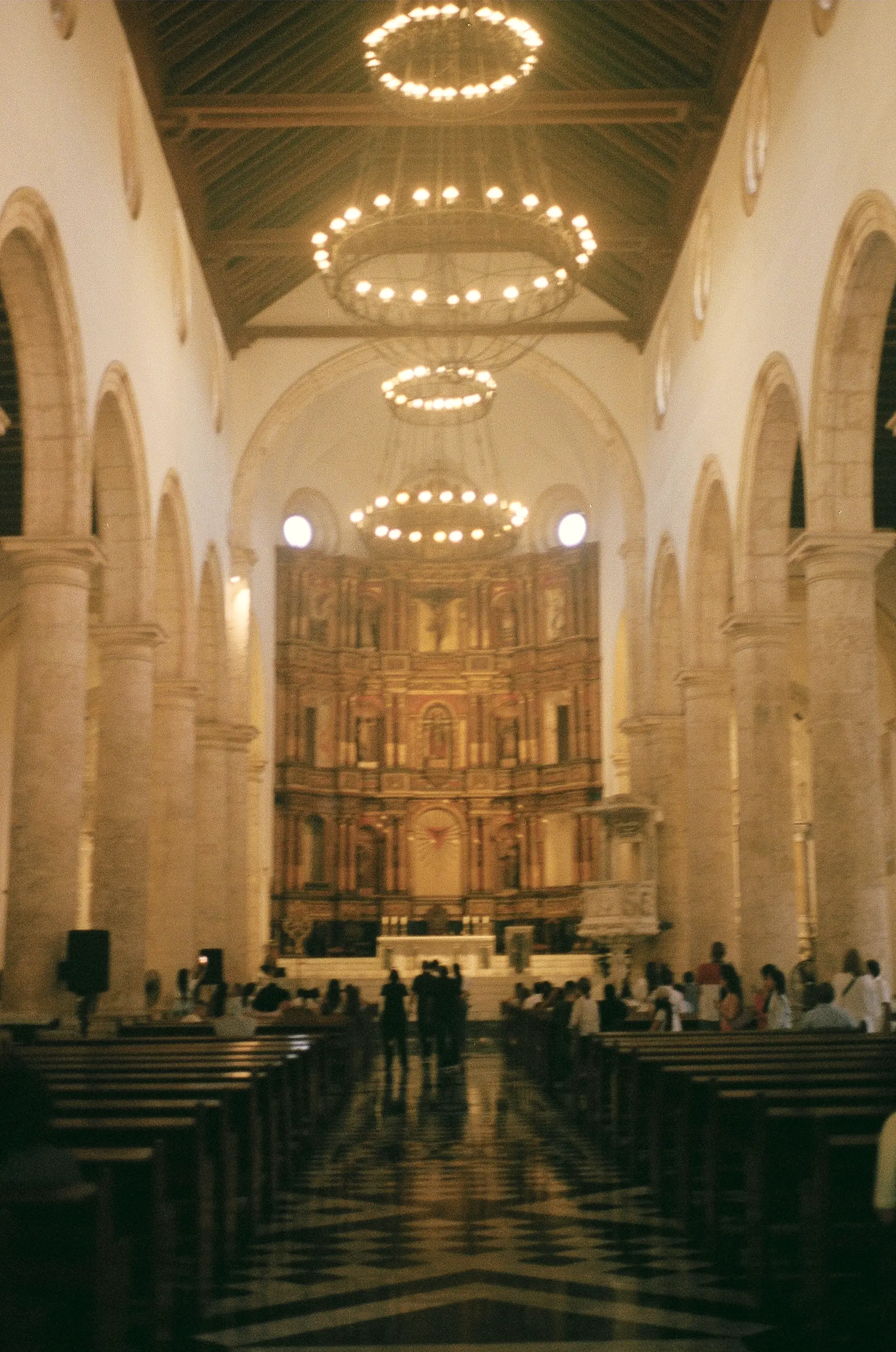 Church nave with circular chandeliers, a gilded altarpiece and pews