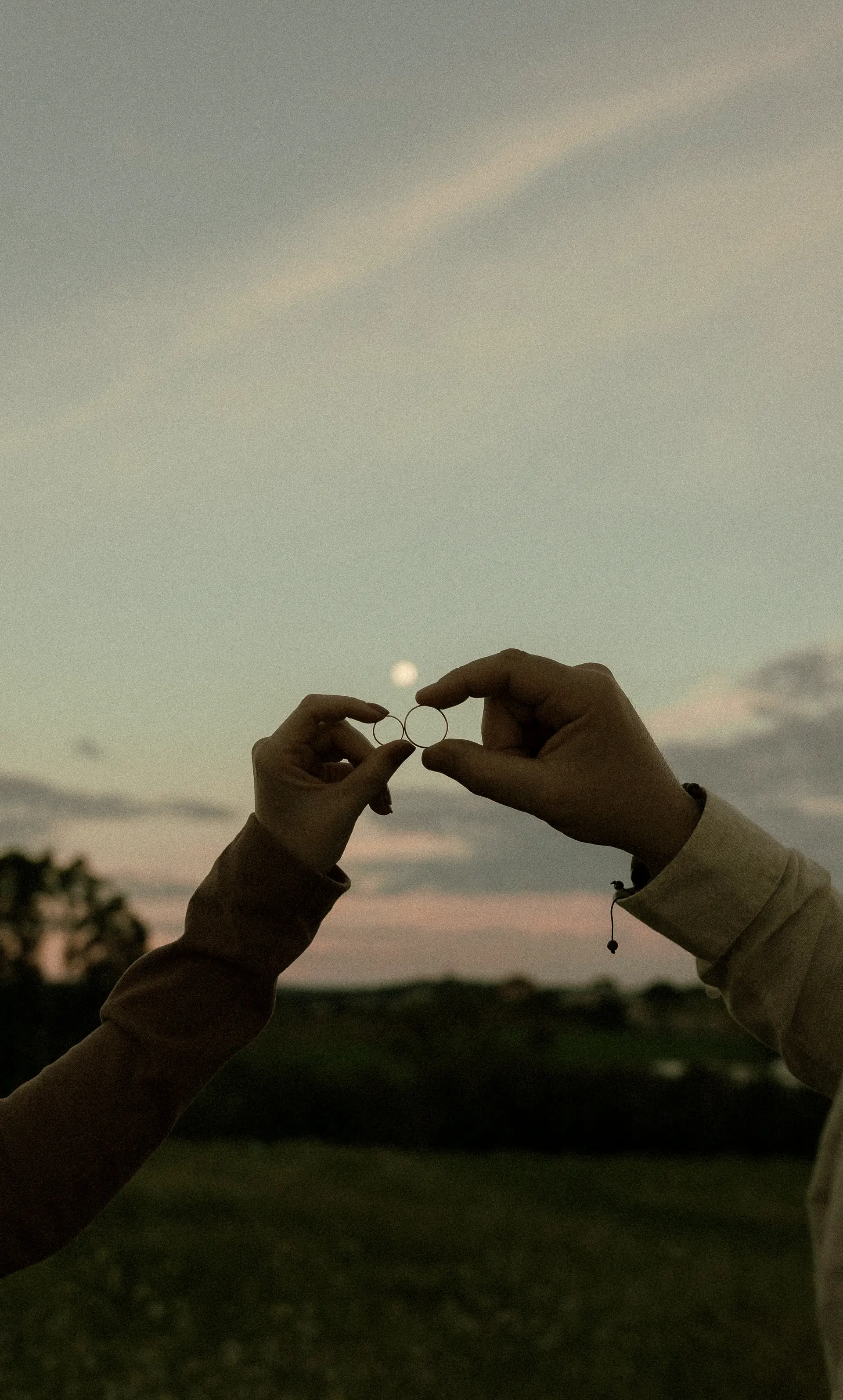 Two hands holding a ring against the evening sky