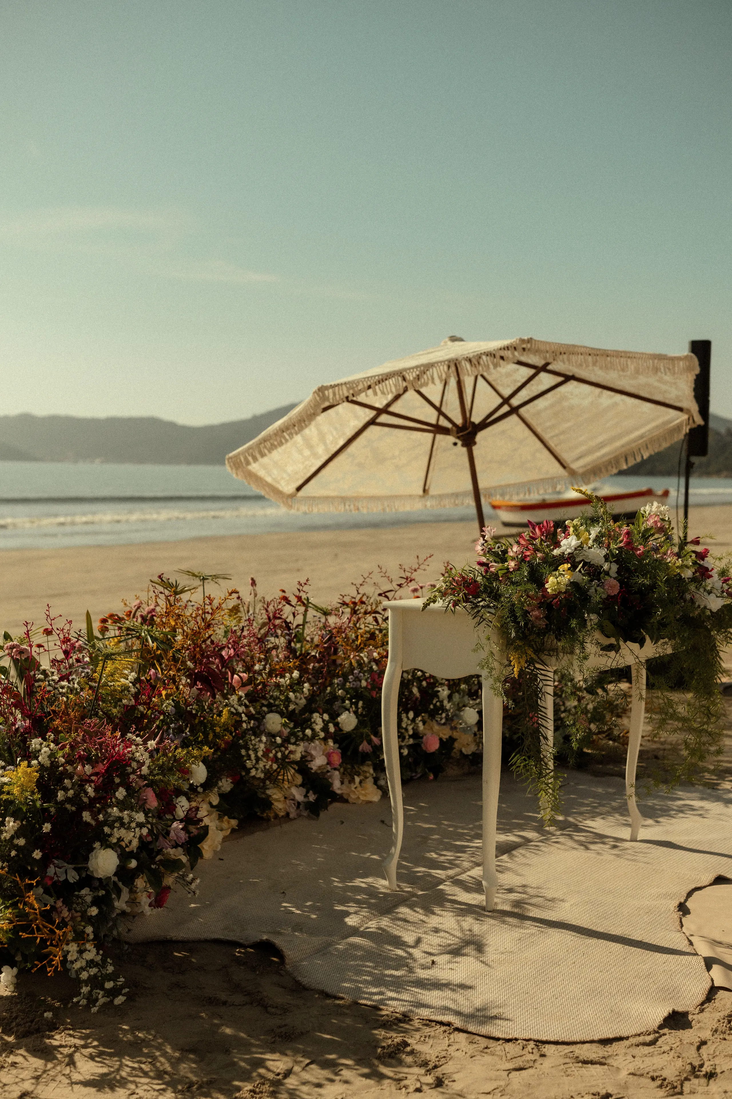 Beach setup with a table of wildflowers and a white umbrella