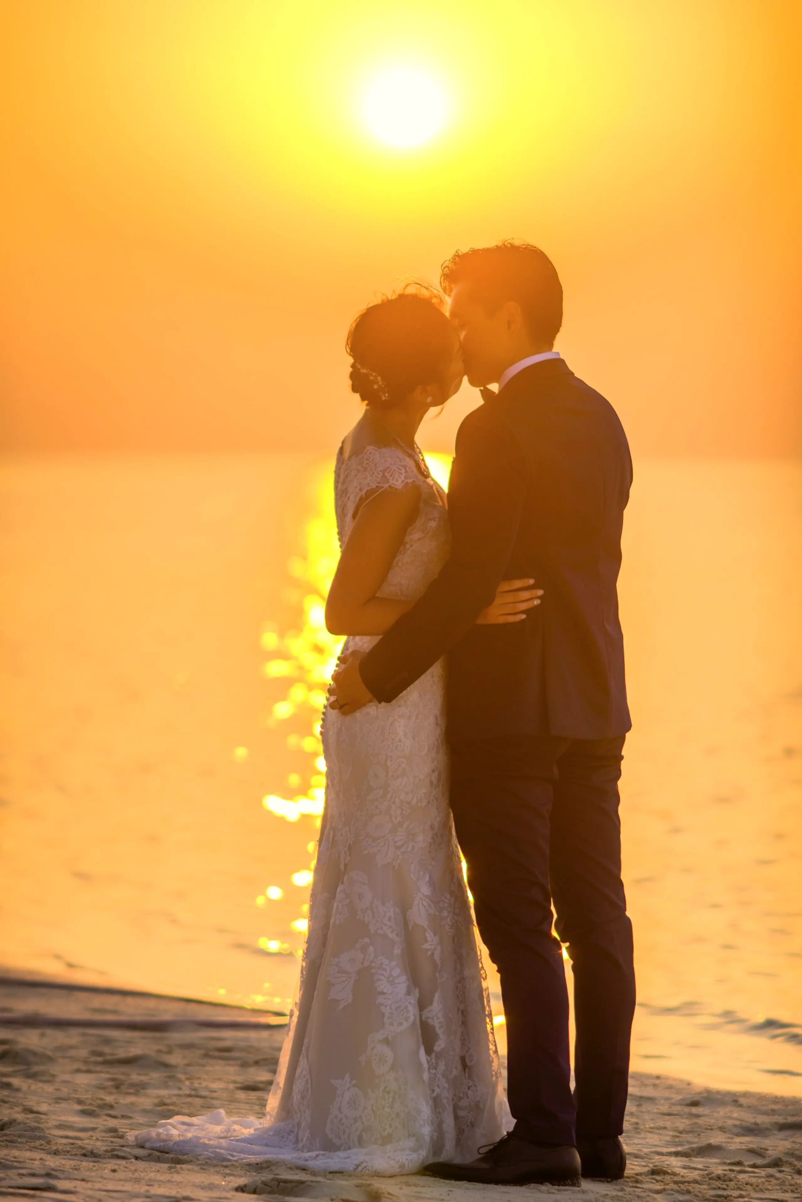 Newlyweds kissing by the sea with the sun low on the horizon