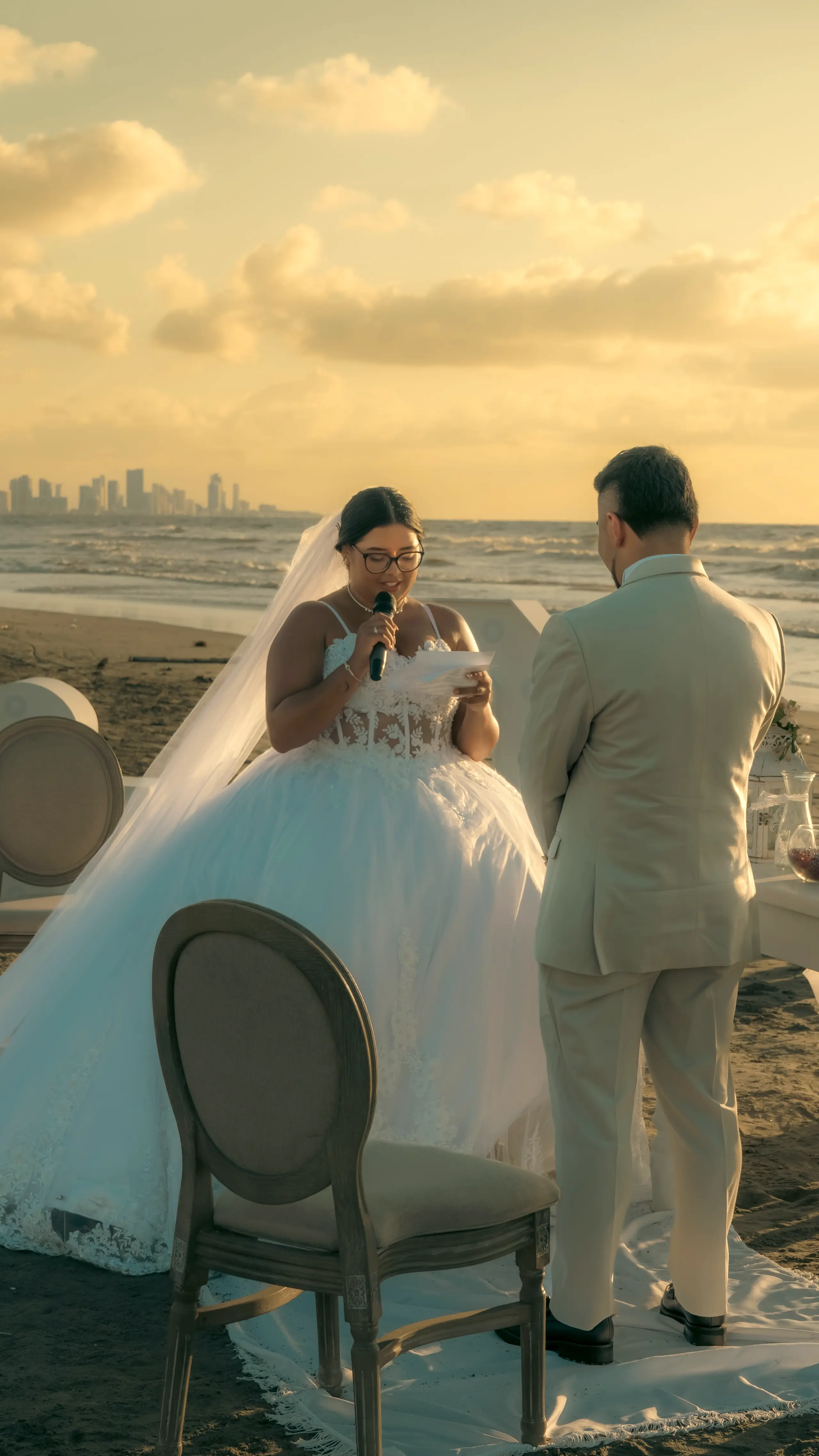 Newlyweds by the sea at sunset with a city skyline in the distance