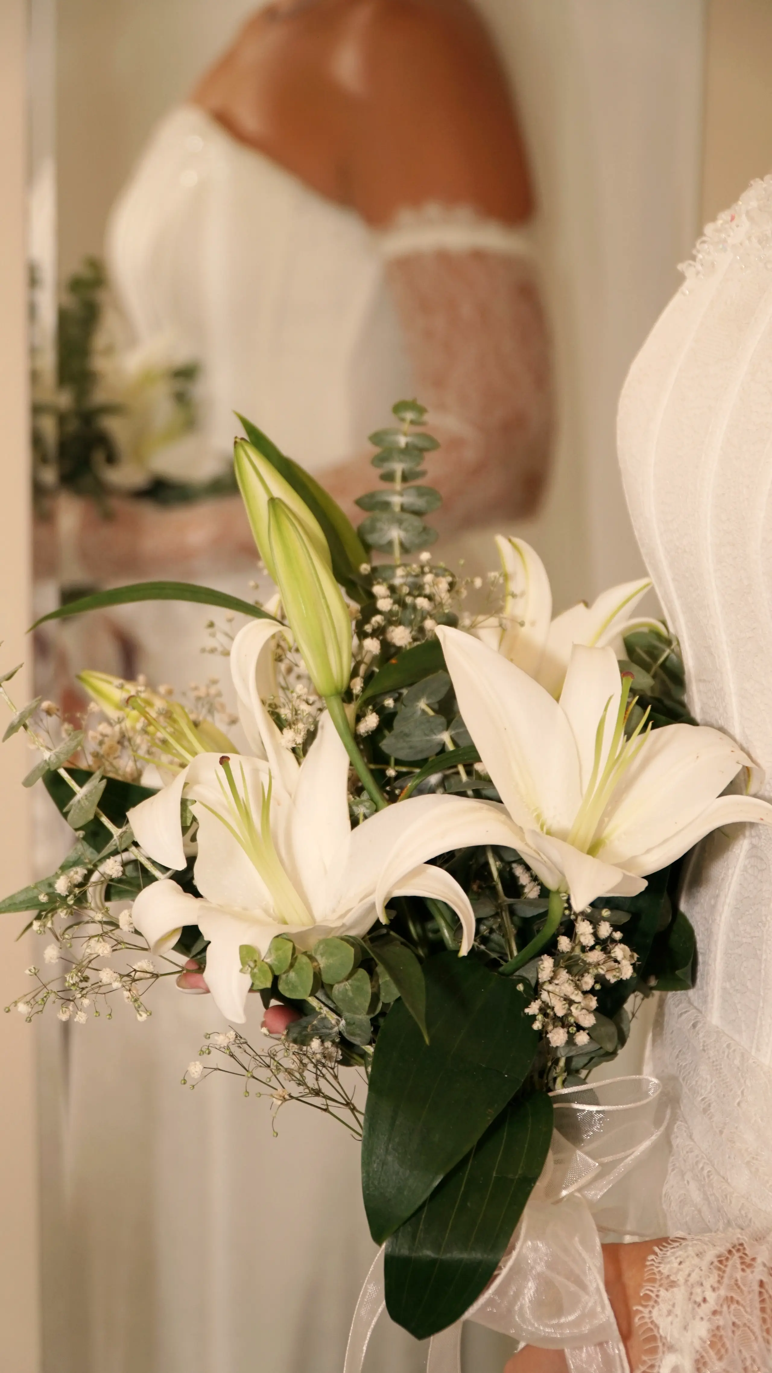 Bouquet of white lilies and foliage beside the bride's dress