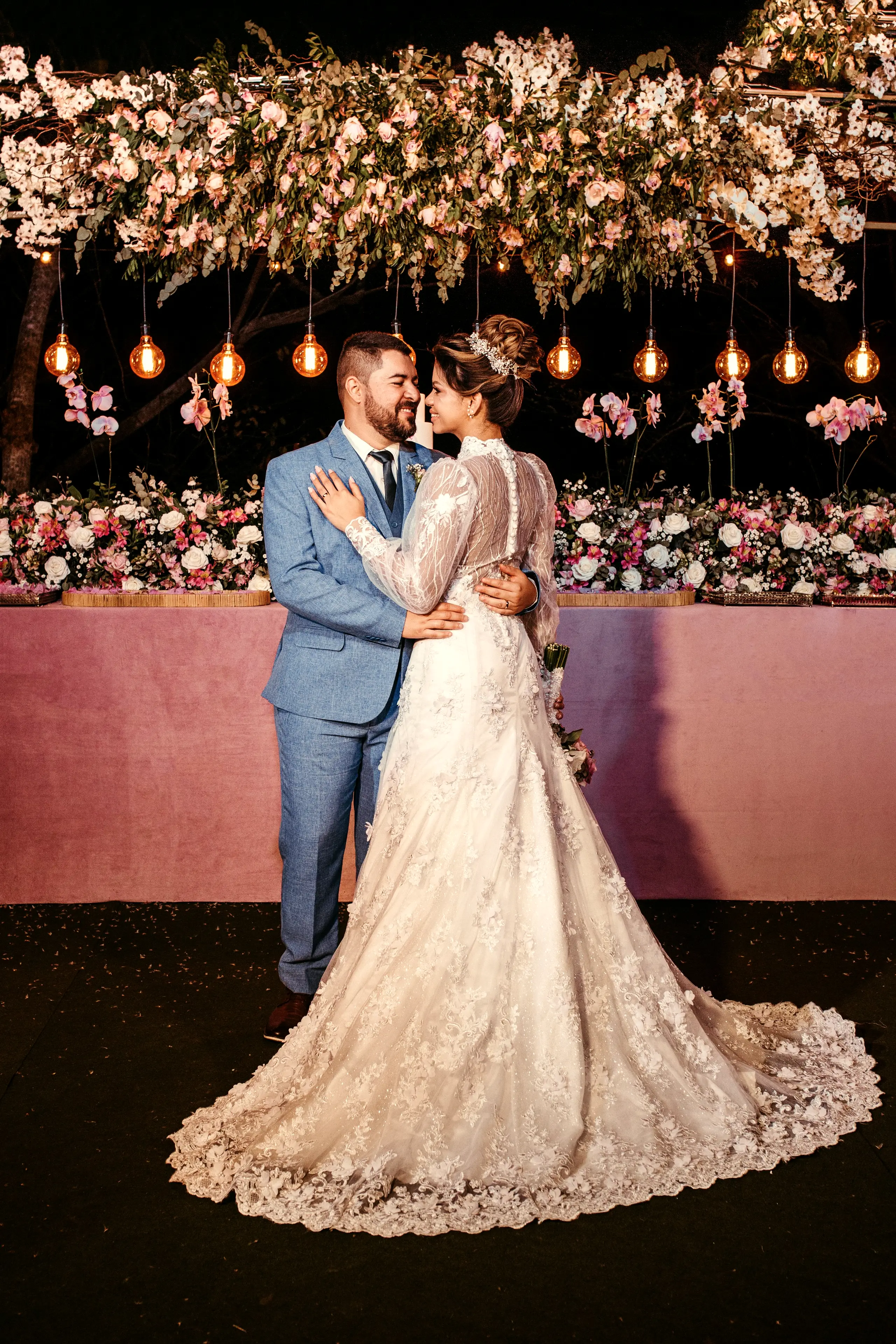Newlyweds embracing under a canopy of flowers and warm lights at night