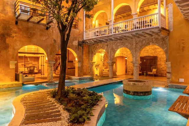 Colonial courtyard lit at night with a pool, arches and a tree at its center