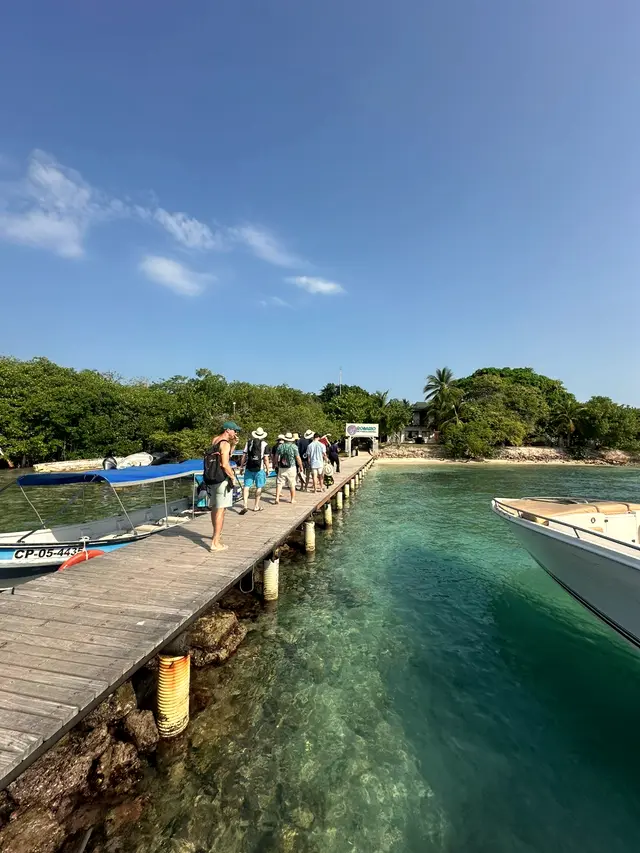 Wooden pier over clear green water with a boat, for arriving at the island