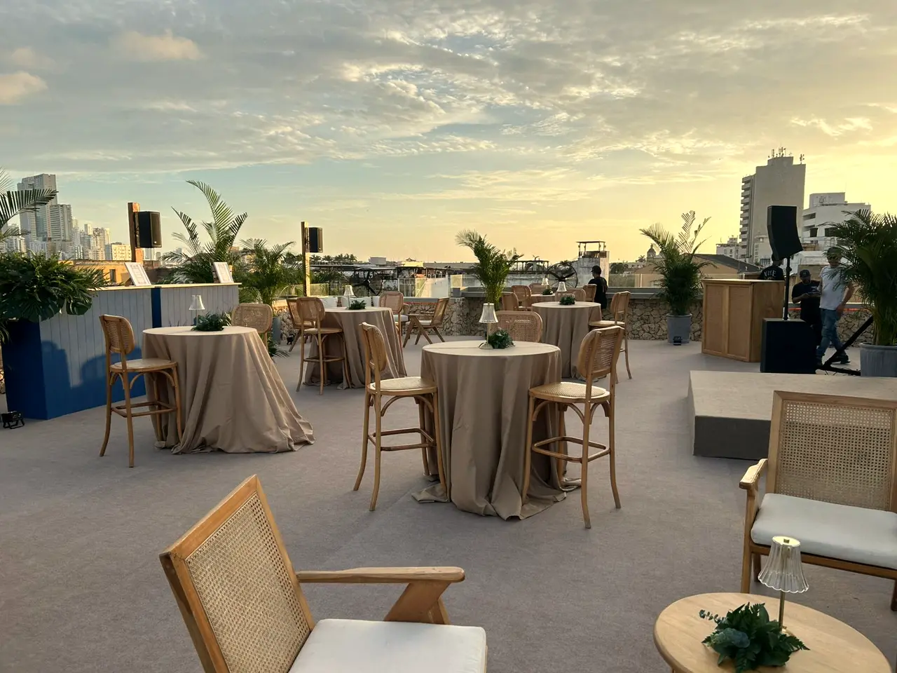 Rooftop terrace at dusk with high tables and rattan armchairs, the city beyond
