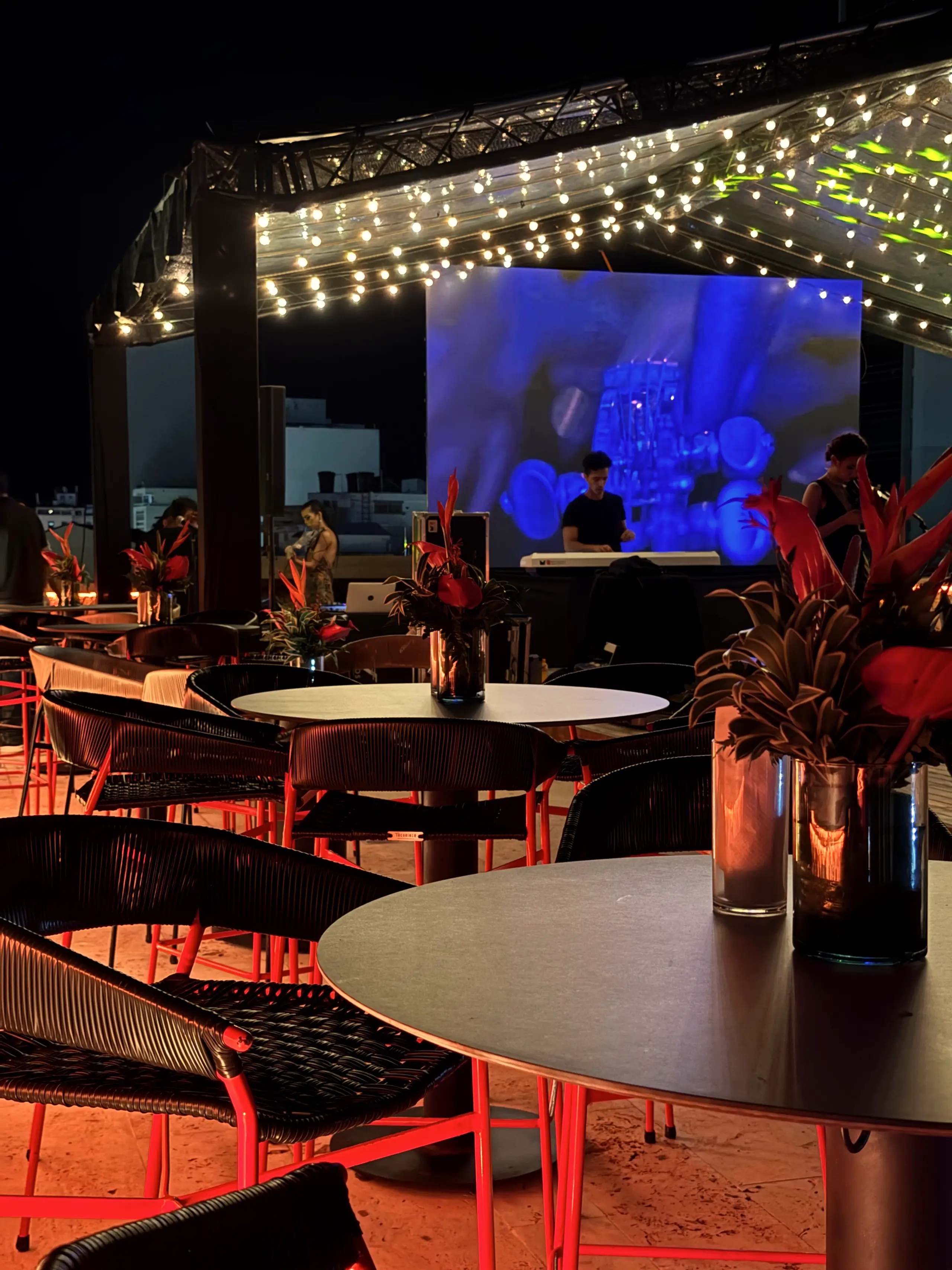 Terrace at night with tables, tropical flower centerpieces and a blue screen behind
