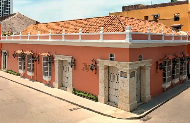 Fachada rosada de una casa colonial de esquina con piedra tallada y ventanas con rejas