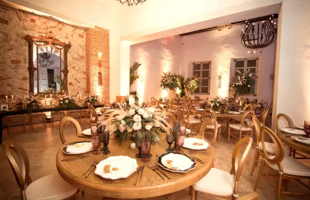 Salón con mesas redondas de madera y un espejo antiguo sobre un muro de piedra
