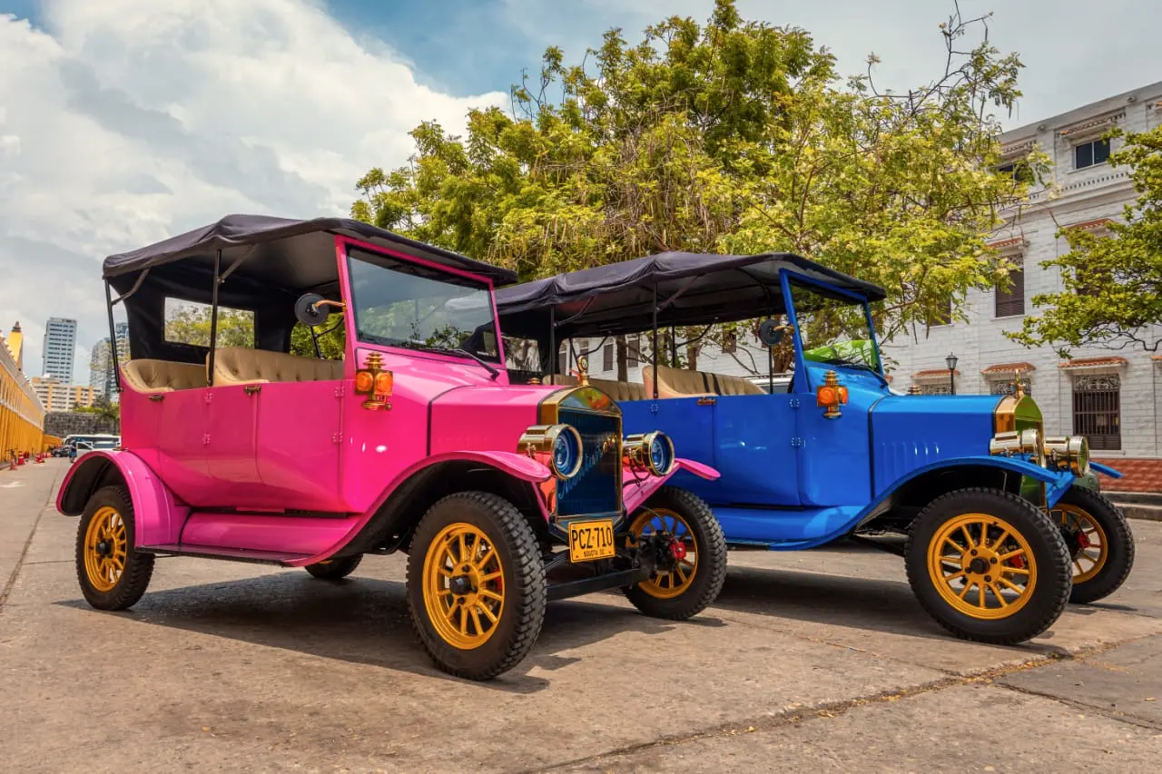 Two vintage cars, one pink and one blue, parked in a plaza