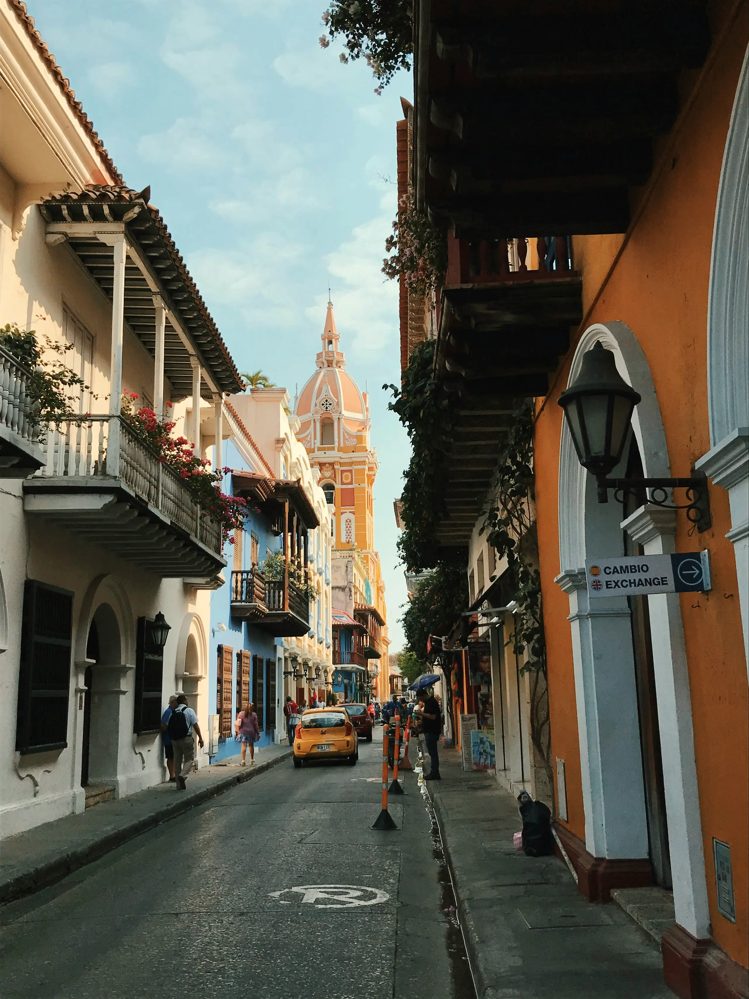 Historic-center street with wooden balconies and a yellow taxi