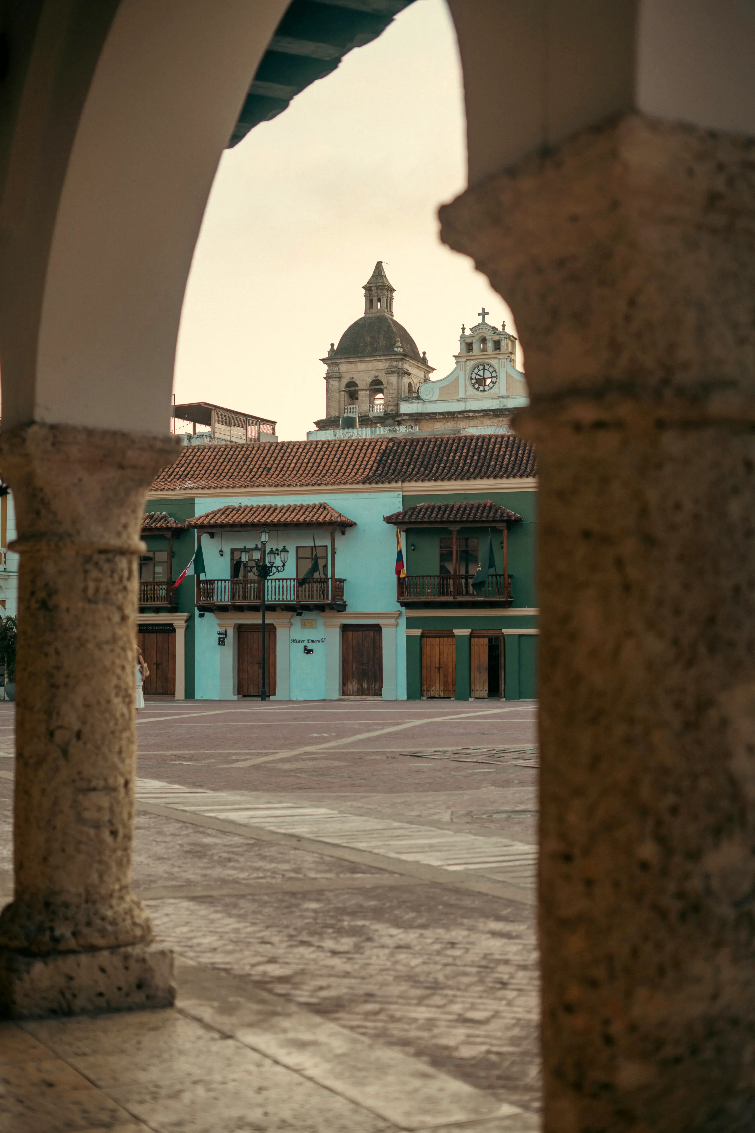 Plaza seen through stone arches, with colorful houses beyond