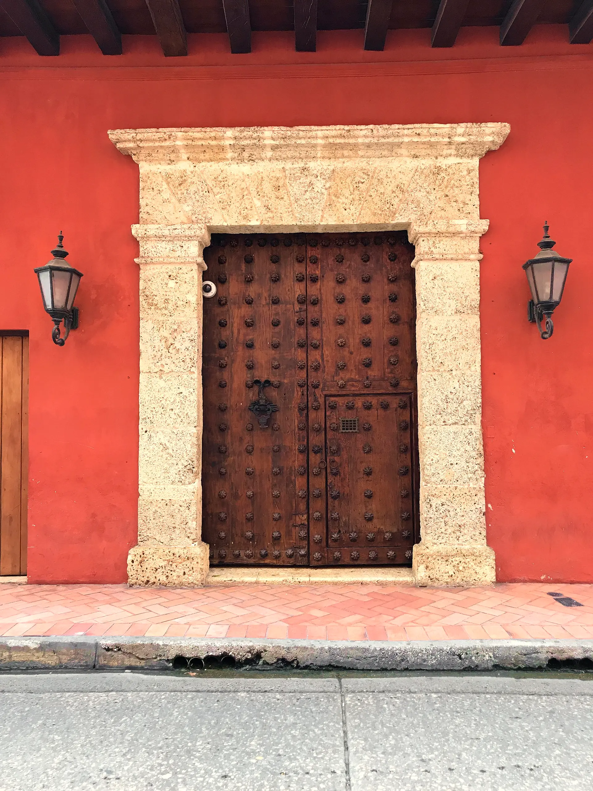 Wooden door with ironwork in a red wall between two lanterns