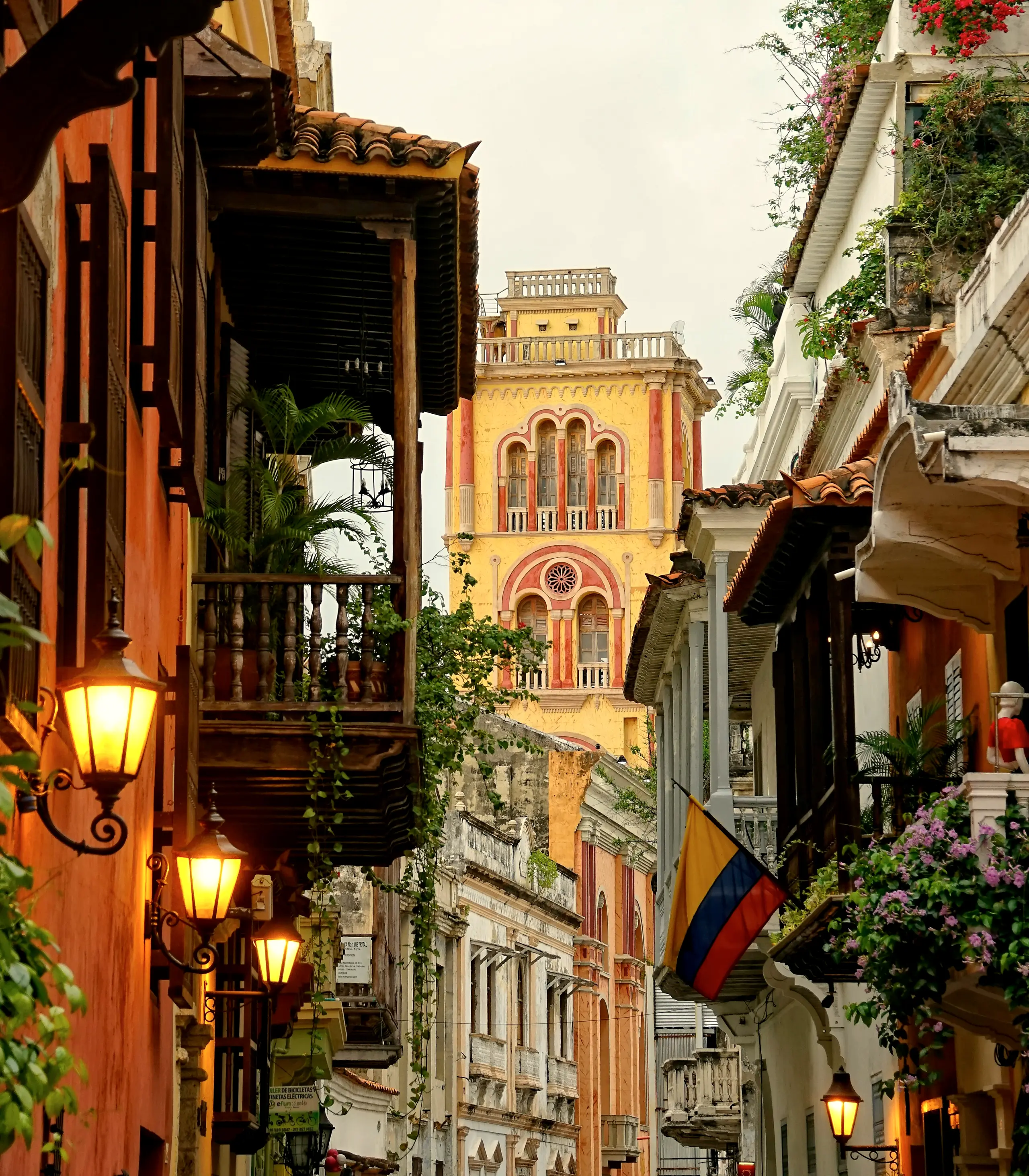 Street with lit lanterns and a church tower in the distance