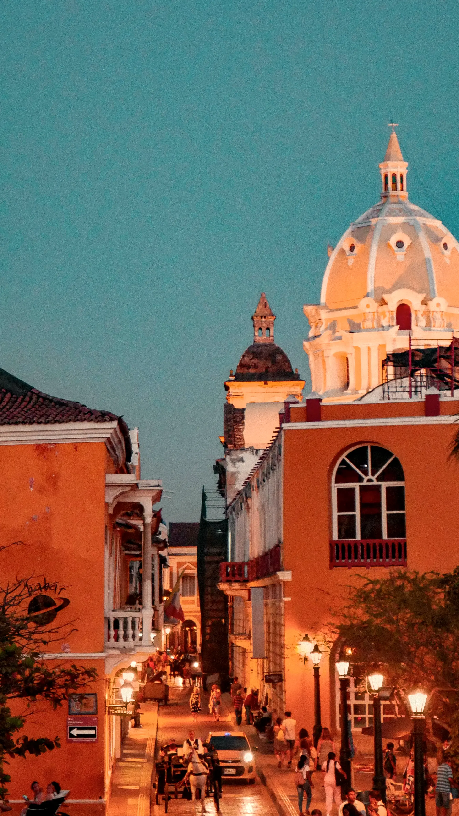 Historic-center street at dusk with lit lamps and a dome beyond
