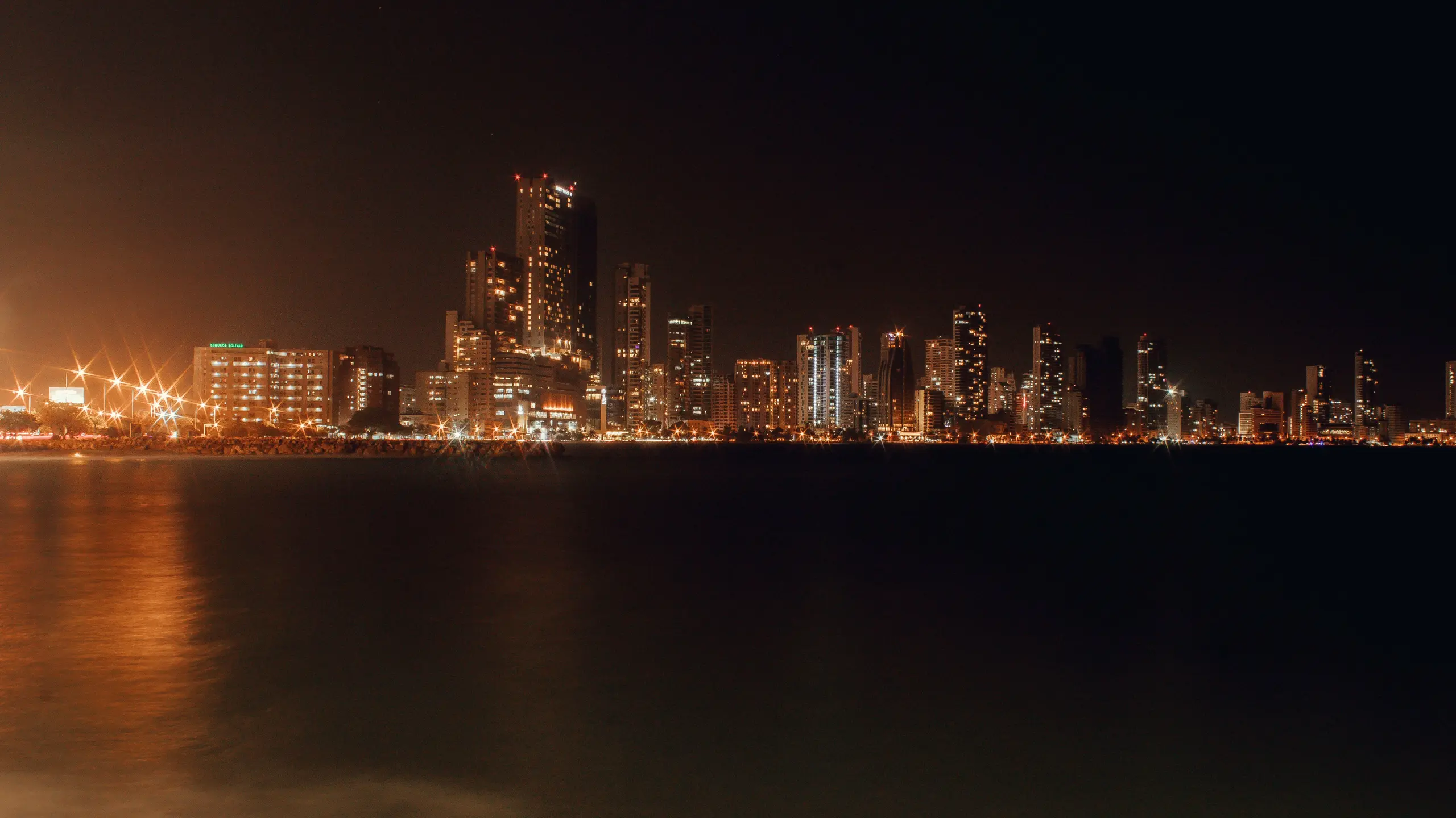 Skyline of lit buildings by the sea at night