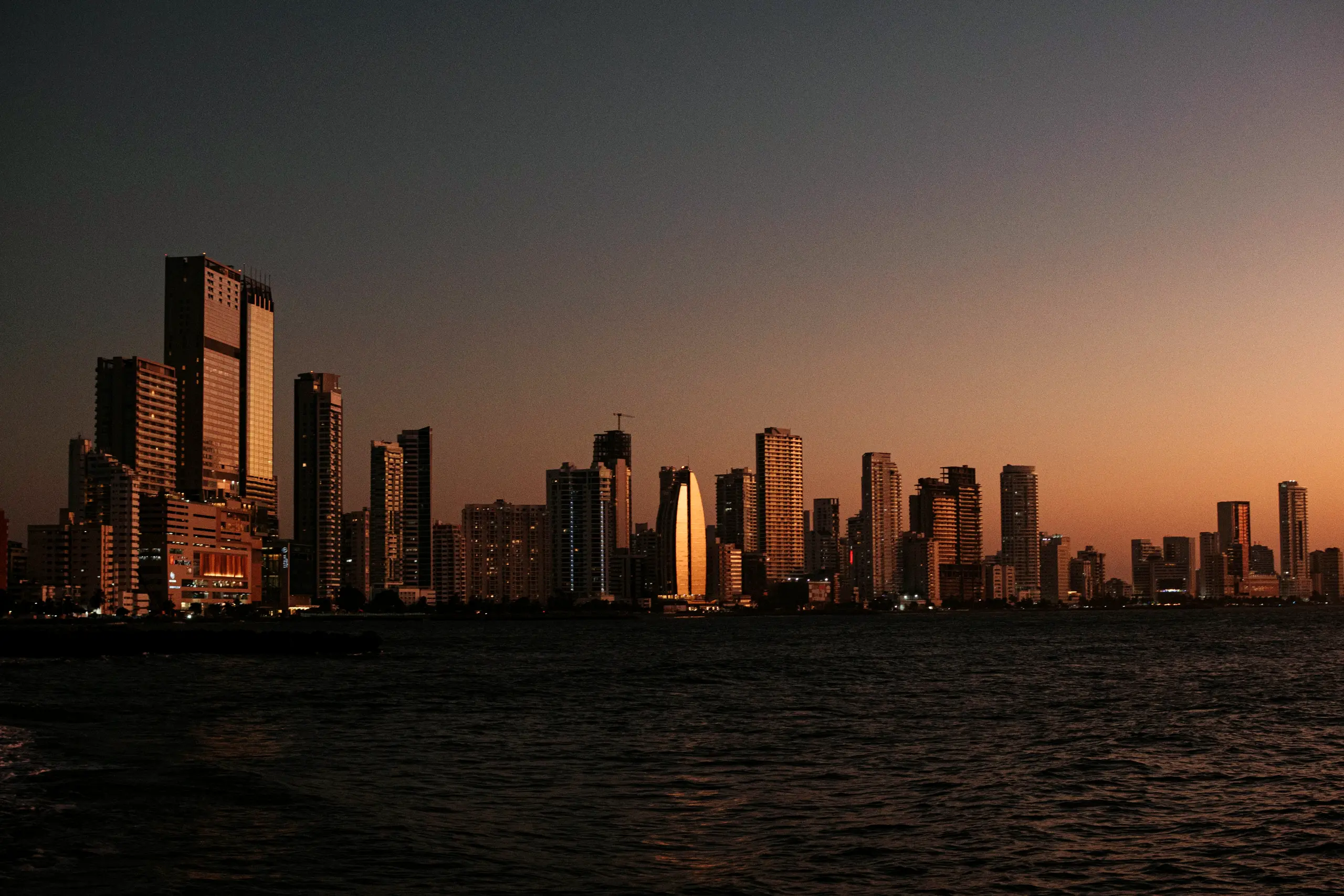 High-rise buildings over the sea at dusk with warm light on the horizon