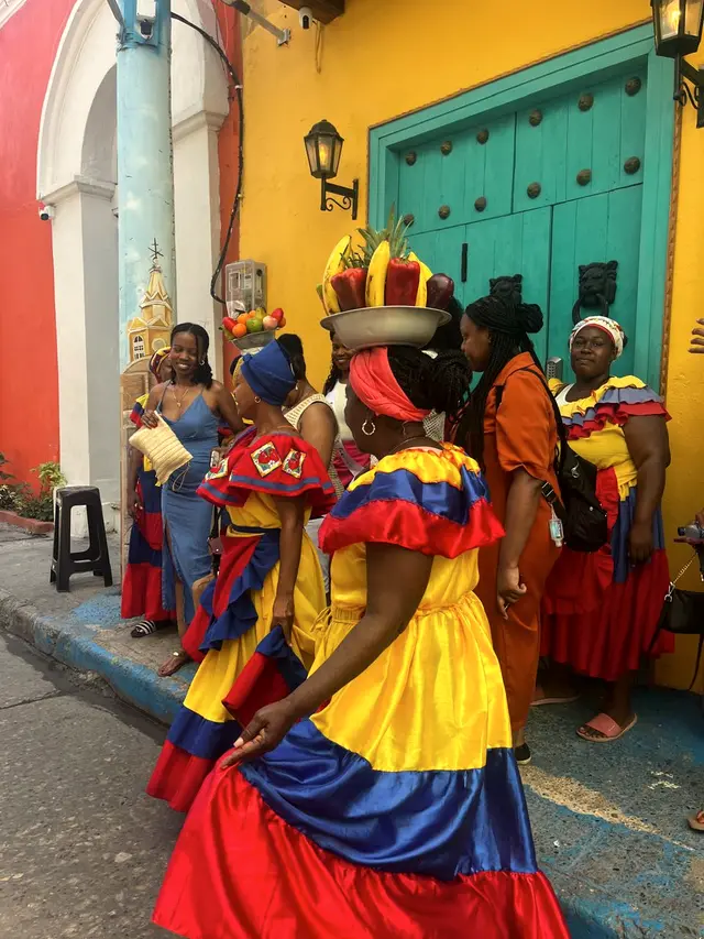Women in traditional yellow, blue and red dresses in front of a turquoise door