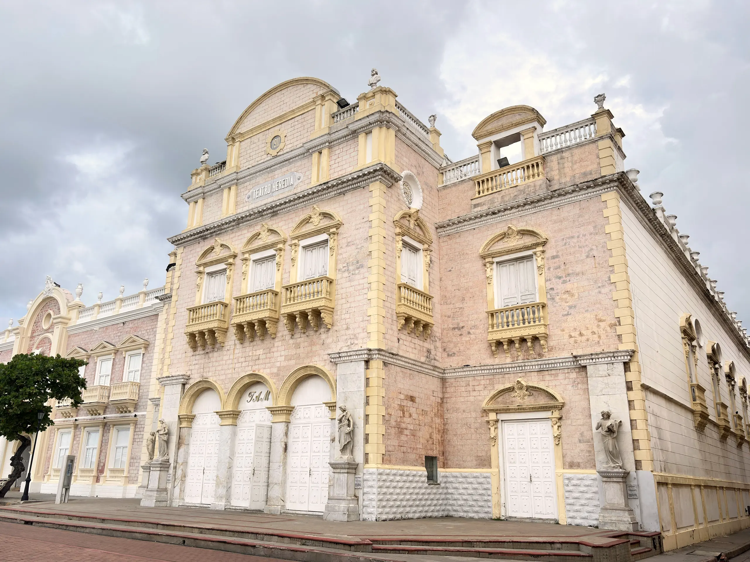Facade of the Teatro Heredia in pale stone under a cloudy sky