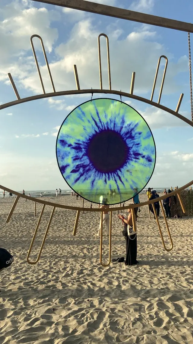 Eye-shaped sculpture with blue and green stained glass on the beach sand