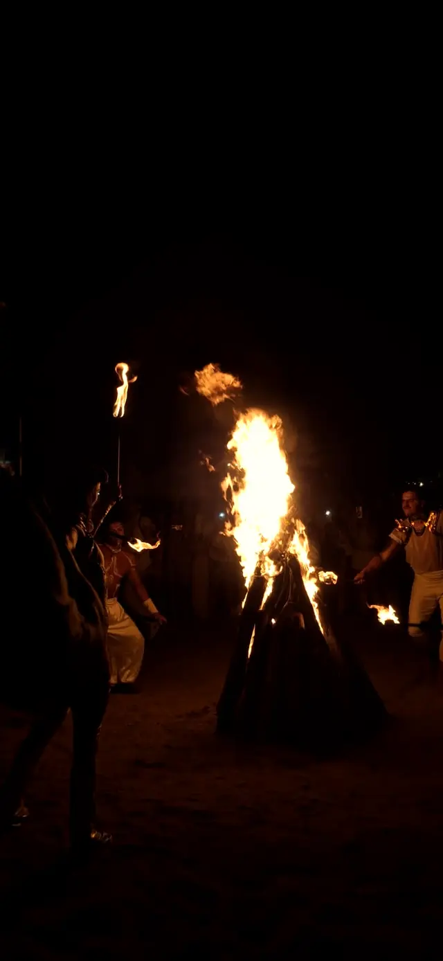 Fire dancer with torches beside a bonfire on the beach at night