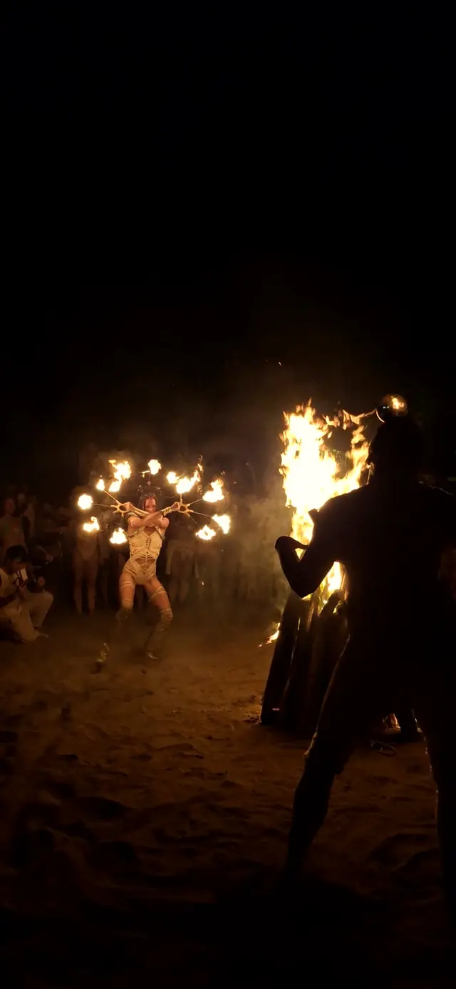 Lit bonfire and performers on the beach at night