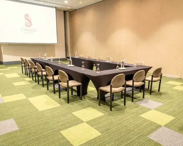 Sala de reuniones con mesas en U y pantalla de proyección