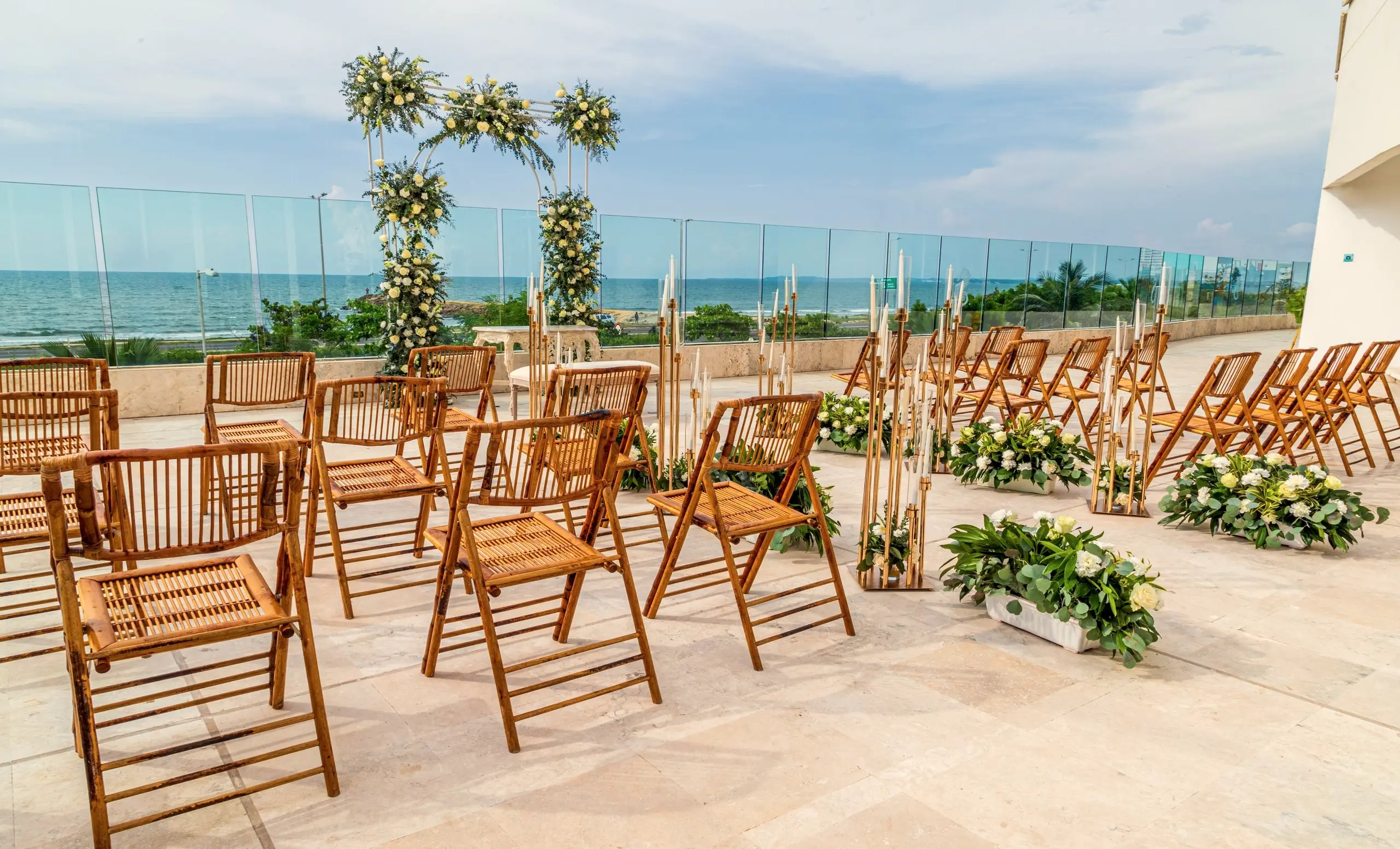 Terraza frente al mar con sillas de madera y arreglos de flores para un evento al aire libre