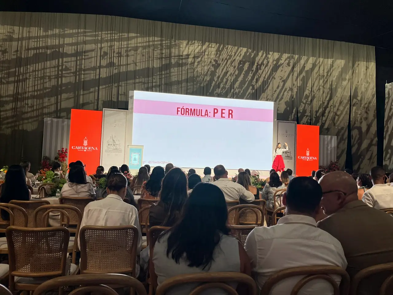 Auditorium with a red stage and seated audience at a convention