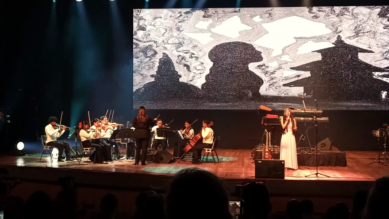 Chamber orchestra and soloist on a stage with a black-and-white projection