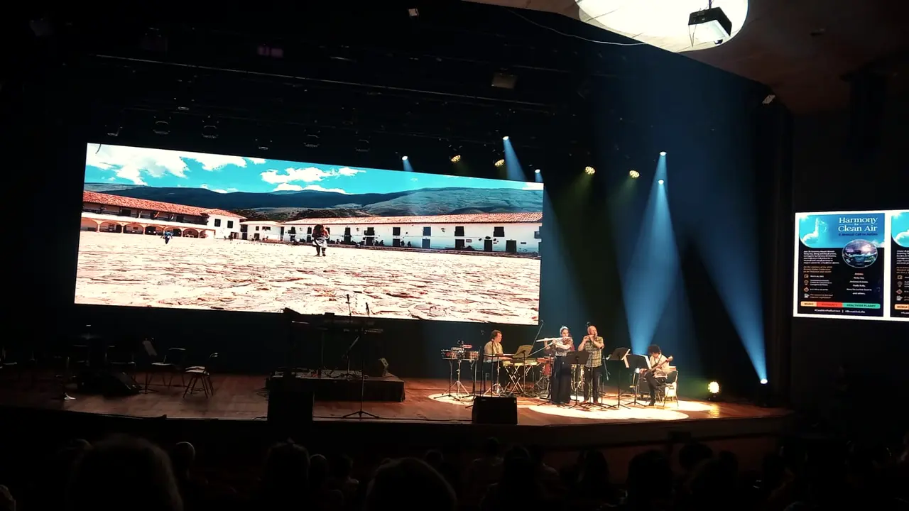 Stage with musicians and a panoramic screen showing a colonial square