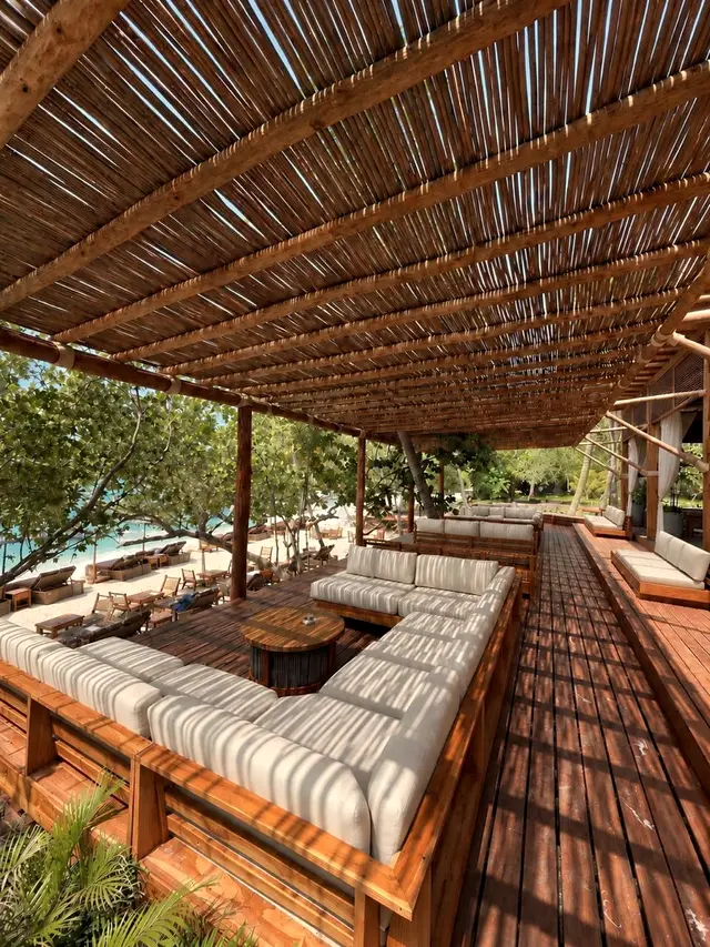 Open lounge with white sofas and a cane roof over a wooden deck