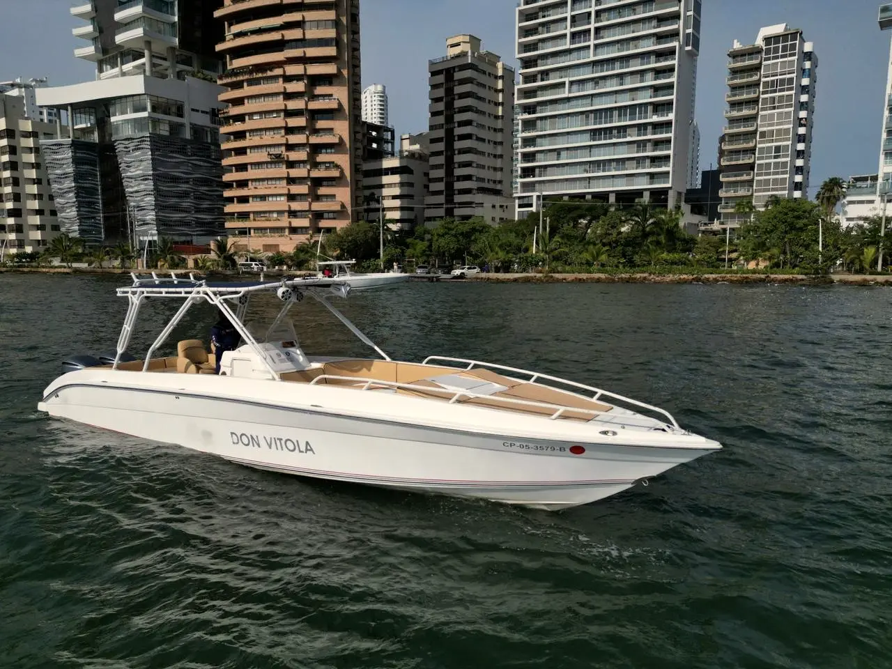 White boat with a wide deck in front of high-rise coastal buildings
